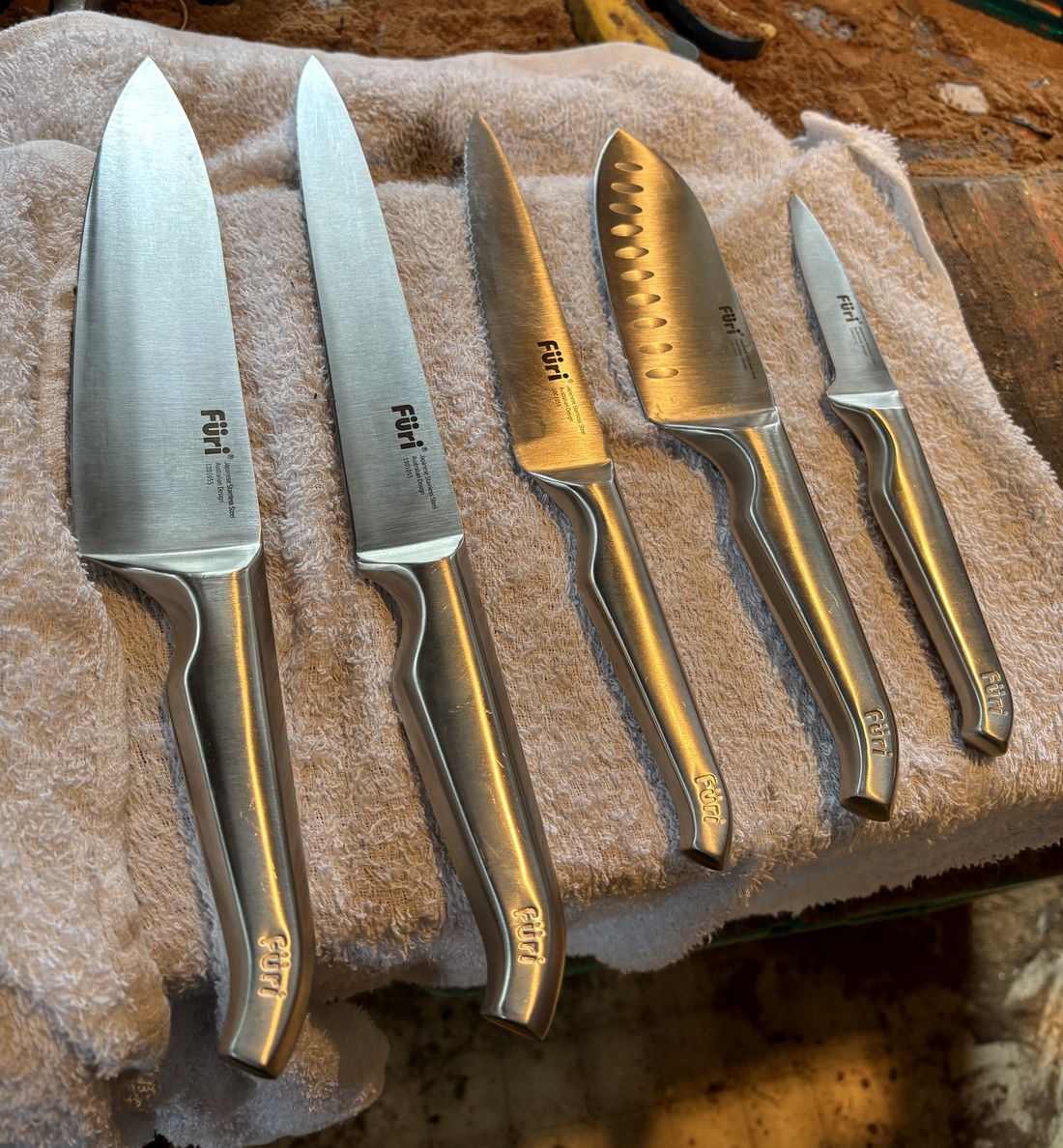 Five freshly sharpened kitchen knives laid out on a towel